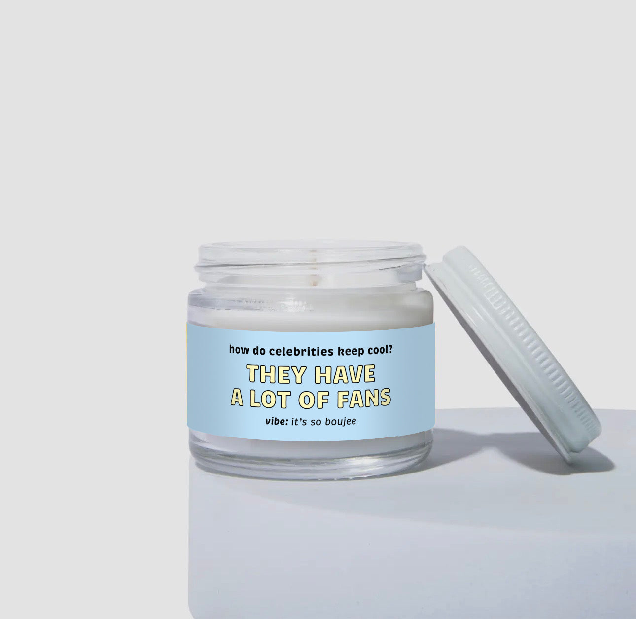 2 oz mini candle in a clear glass jar with coconut soy wax and a light blue label. The label reads “They Have A Lot of Fans” with the question “How do celebrities keep cool?” above it. The scent vibe is described as “it’s so boujee.