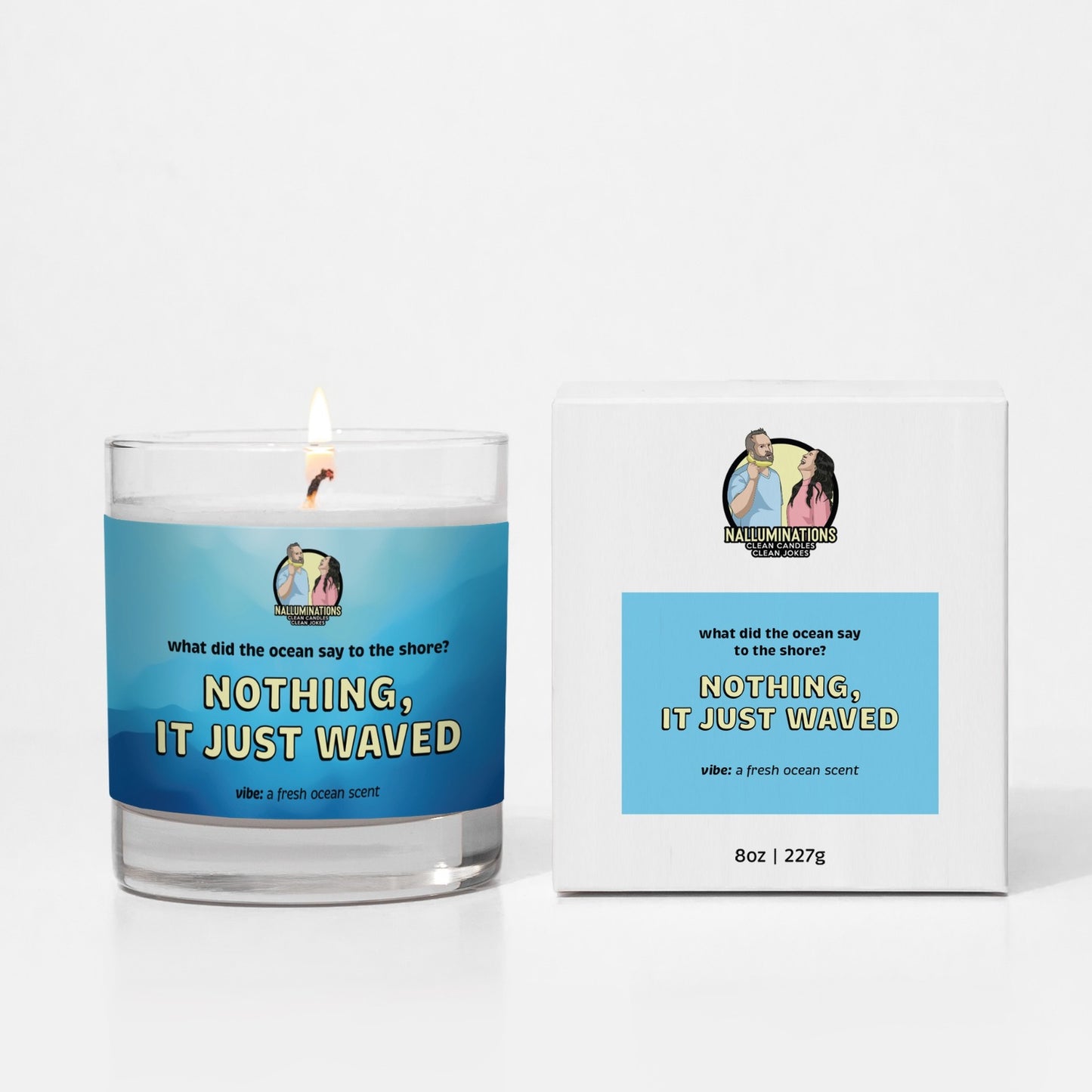 8oz coconut soy candle shown lit in a clear glass jar with a blue label that reads “Nothing, It Just Waved.” Comes with a matching box. Fresh ocean scent, placed on a white background.