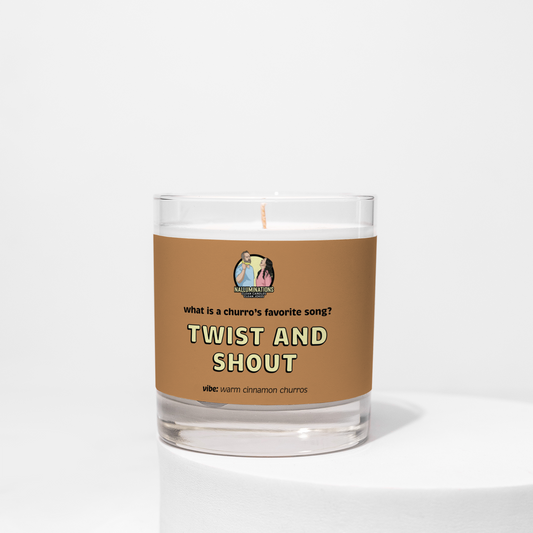 8oz coconut soy candle in a clear glass jar with a brown label that reads “What is a churro’s favorite song? Twist and Shout.” The scent vibe is warm cinnamon churros. The candle is unlit and placed against a white background.