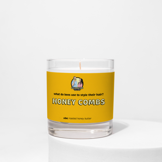 8oz coconut soy candle in a clear glass jar with a yellow label that reads “What do bees use to style their hair? Honey Combs.” The scent vibe is roasted honey butter. The candle is unlit and placed against a white background.