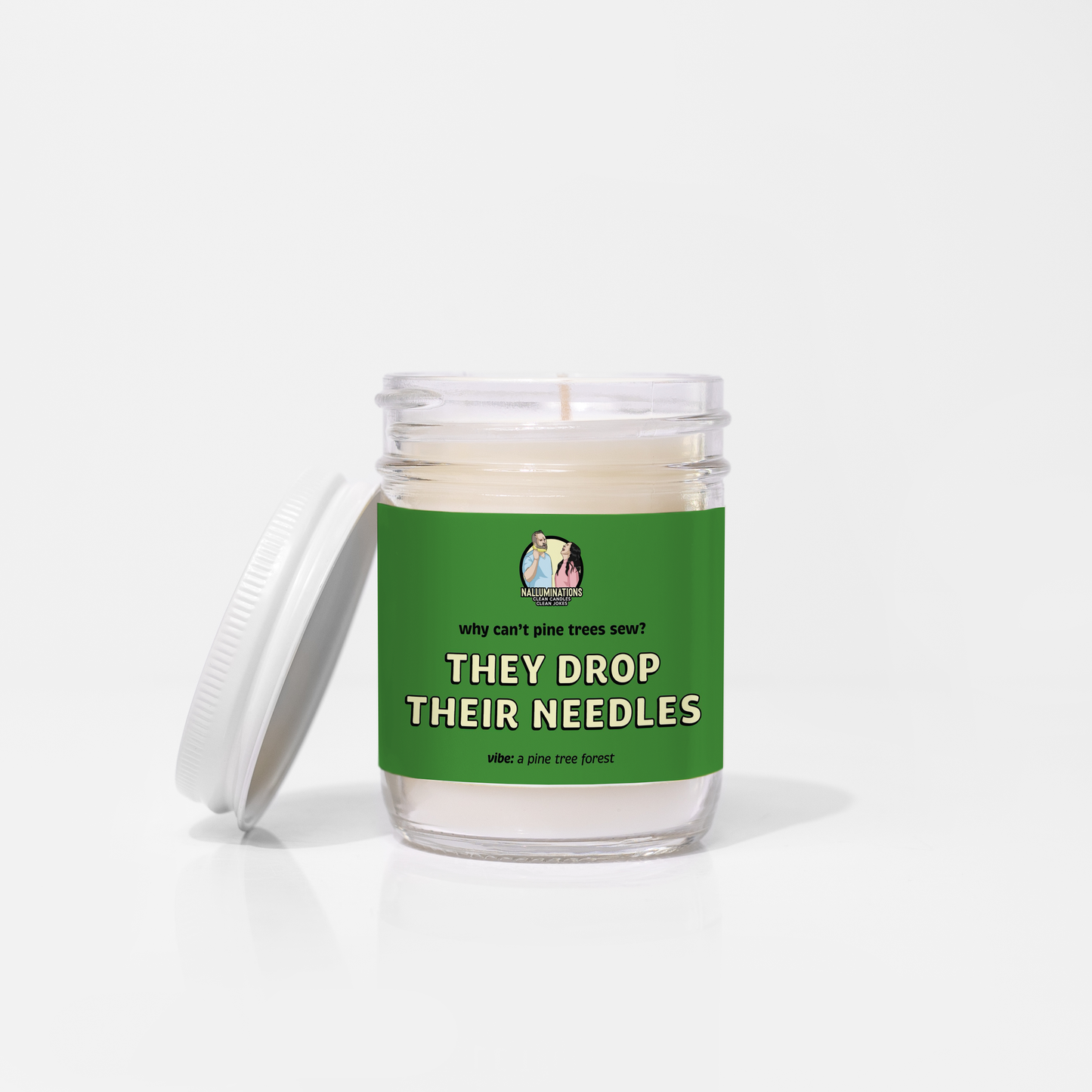 6.5oz coconut soy candle in a clear glass jar and white metal lid with a green label. Label says, “Why can’t pine trees sew? They drop their needles.” Pine tree forest fragrance, shown on a white background.