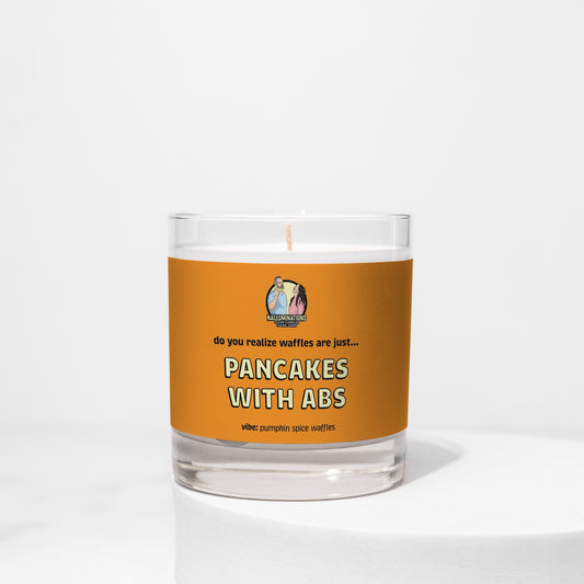 8oz coconut soy candle in a clear glass jar with a bright orange label that reads “Pancakes With Abs – Pumpkin Spice Waffles.” The candle is unlit and displayed on a white background.
