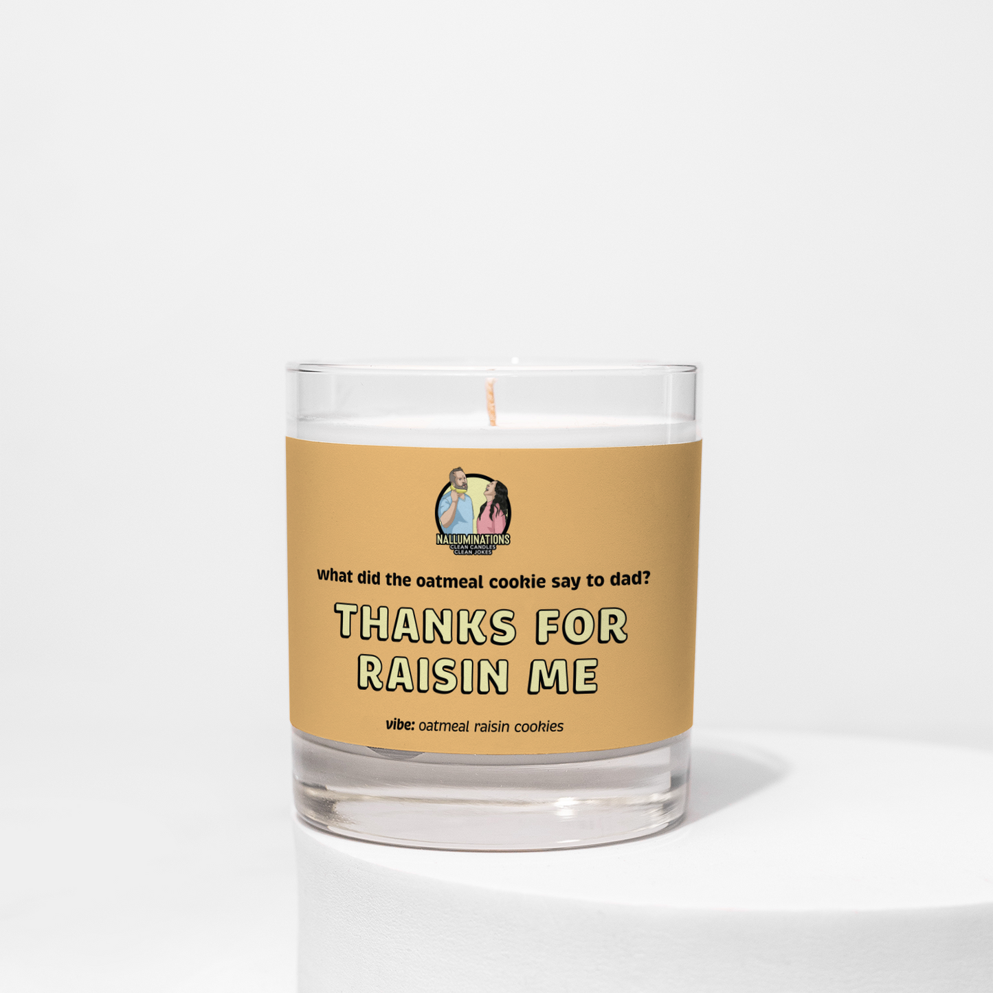 Unlit 8oz glass jar coconut soy candle with a light tan label that says: 'What did the oatmeal cookie say to dad? THANKS FOR RAISIN ME.' Scent note reads: 'vibe: oatmeal raisin cookies.'