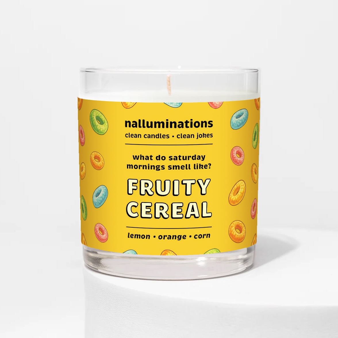 Nalluminations 8oz coconut soy candle in a clear glass vessel with a yellow label  and text "fruity cereal" featuring colorful cereal graphics on a white background