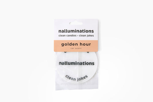 A packaged car scent disc from the brand nalluminations, labeled 'golden hour car scent'. The product consists of a white circular disc with black text, sealed in a clear plastic sleeve with a white and peach paper header card.
